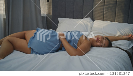 Young Woman Lying Across Bed in Sunny Bedroom Opposite Window 131381247