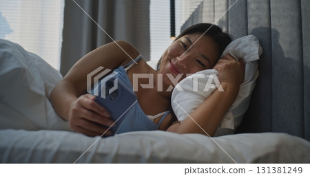 Young Women Lies in bed Scrolls Through News Feed on Smartphone and Happily Smiles 131381249