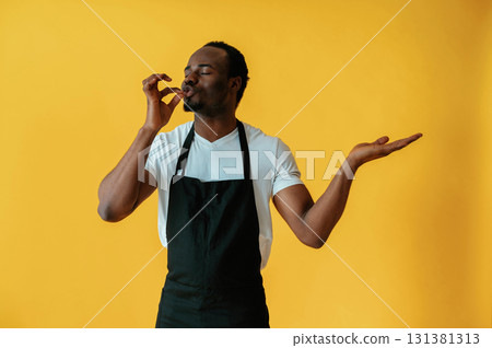 Cafe worker. Black man is in the studio against yellow background Cafe worker. Black man is in the studio against yellow background 131381313