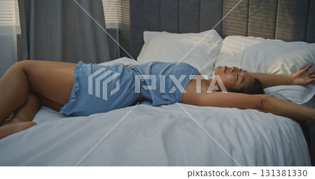 Young Woman Lying Across Bed in Sunny Bedroom Opposite Window 131381330