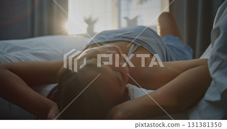 Young Woman in Blue Pajamas Basking in Bright Sunlight, Running Hands Through Hair Young Woman in Blue Pajamas Basking in Bright Sunlight, Running Hands Through Hair 131381350