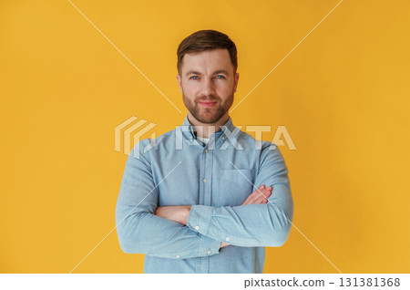 Standing with arms crossed. Attractive man in blue shirt is against yellow background Standing with arms crossed. Attractive man in blue shirt is against yellow background 131381368