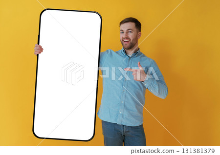 Big smartphone, place for copy space. Attractive man in blue shirt is against yellow background 131381379