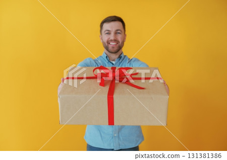 Giving present, gift box. Attractive man in blue shirt is against yellow background 131381386