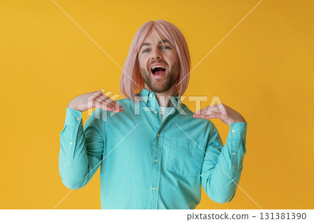 Making facial expression, hand gestures. Guy with pink hair is posing against yellow background Making facial expression, hand gestures. Guy with pink hair is posing against yellow background 131381390