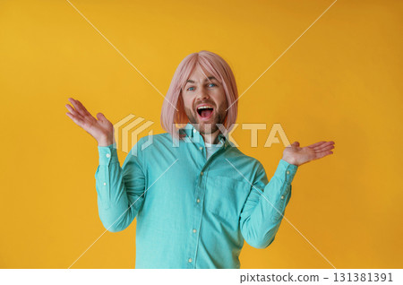 Making facial expression, hand gestures. Guy with pink hair is posing against yellow background Making facial expression, hand gestures. Guy with pink hair is posing against yellow background 131381391