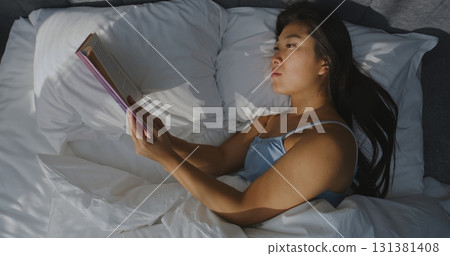 Beautiful Young Woman Reading Book in Bed in Bedroom 131381408