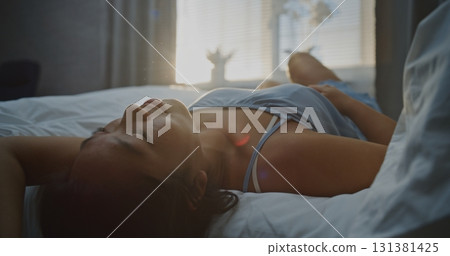 Young Woman in Blue Pajamas Basking in Bright Sunlight, Running Hands Through Hair 131381425
