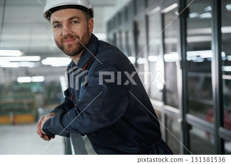 Leaning on the railings. Factory worker is indoors with hard hat Leaning on the railings. Factory worker is indoors with hard hat 131381536