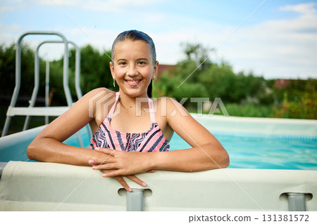 Teen girl enjoying a summer day by the pool with a cheerful smile and relaxed demeanor in a sunny outdoor setting 131381572