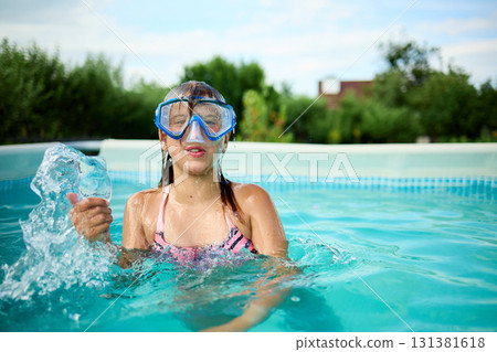 Girl enjoying a refreshing swim in a backyard pool while wearing a snorkel during a sunny summer day 131381618