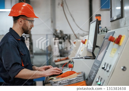 Side view, operating the machine. Factory worker is indoors with hard hat 131381638