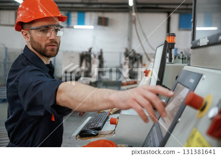Side view, operating the machine. Factory worker is indoors with hard hat Side view, operating the machine. Factory worker is indoors with hard hat 131381641