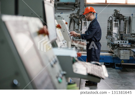 View from the side, working with machine, operator. Factory worker is indoors with hard hat View from the side, working with machine, operator. Factory worker is indoors with hard hat 131381645