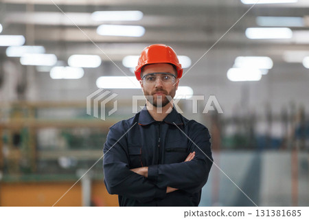 Focused portrait, in glasses. Factory worker is indoors with hard hat Focused portrait, in glasses. Factory worker is indoors with hard hat 131381685