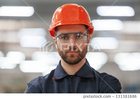 Focused portrait, in glasses. Factory worker is indoors with hard hat Focused portrait, in glasses. Factory worker is indoors with hard hat 131381686
