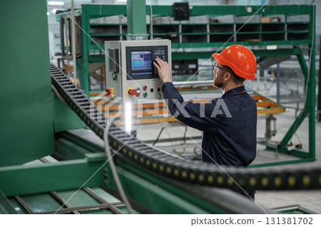 Green colored machine, operator is busy. Factory worker is indoors with hard hat Green colored machine, operator is busy. Factory worker is indoors with hard hat 131381702