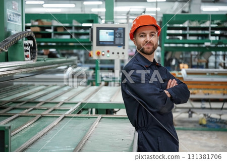 Beautiful man is standing with arms crossed. Factory worker is indoors with hard hat 131381706