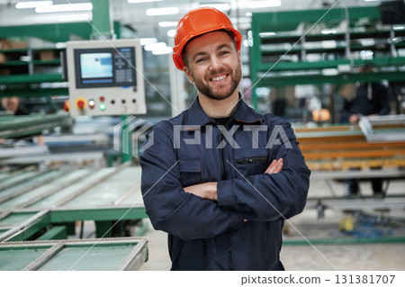 Beautiful man is standing with arms crossed. Factory worker is indoors with hard hat 131381707