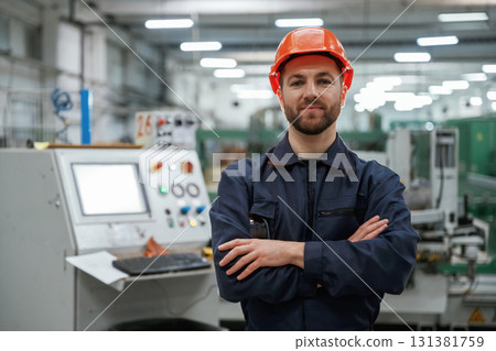 Standing with arms crossed. Factory worker is indoors with hard hat Standing with arms crossed. Factory worker is indoors with hard hat 131381759