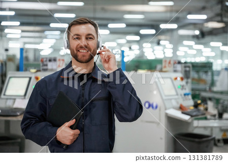 Standing and smiling. Factory worker is indoors with hard hat 131381789