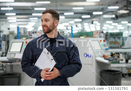 Standing and smiling. Factory worker is indoors with hard hat Standing and smiling. Factory worker is indoors with hard hat 131381791
