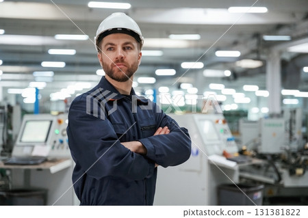 Posing, with arms crossed. Factory worker is indoors with hard hat Posing, with arms crossed. Factory worker is indoors with hard hat 131381822