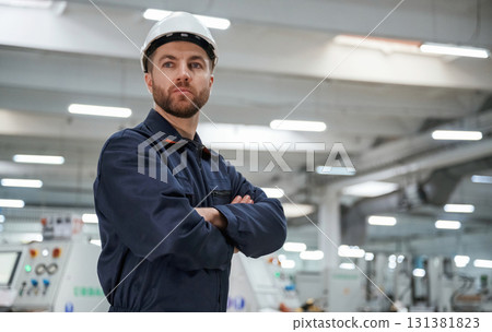 Posing, with arms crossed. Factory worker is indoors with hard hat Posing, with arms crossed. Factory worker is indoors with hard hat 131381823