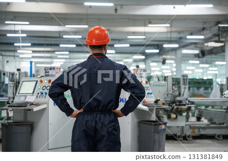 Rear view, standing. Factory worker is indoors with hard hat Rear view, standing. Factory worker is indoors with hard hat 131381849