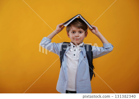 Playing with book, holding it on the head. Little boy is in the studio against yellow background 131382340