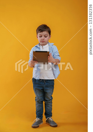 Tablet in hands. Little boy is in the studio against yellow background 131382356