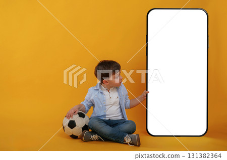 With huge smartphone, copy space place. Little boy is in the studio against yellow background 131382364