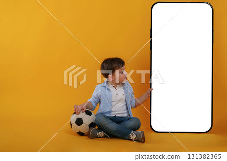 With huge smartphone, copy space place. Little boy is in the studio against yellow background 131382365