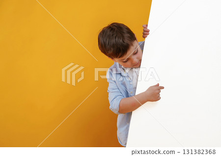 Showing something on the blank white surface. Little boy is in the studio against yellow background Showing something on the blank white surface. Little boy is in the studio against yellow background 131382368