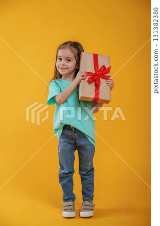 Present in hands, gift box. Cute little girl is against yellow background 131382380