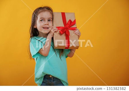 Present in hands, gift box. Cute little girl is against yellow background 131382382