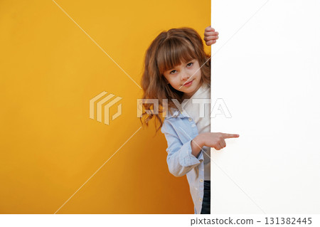 Hiding behind yellow background for copy space. Cute little girl is in the studio Hiding behind yellow background for copy space. Cute little girl is in the studio 131382445