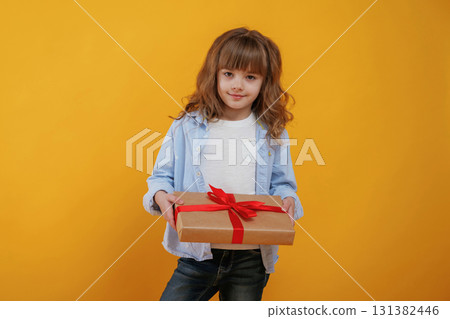 Gift box in hands. Cute little girl is against yellow background 131382446