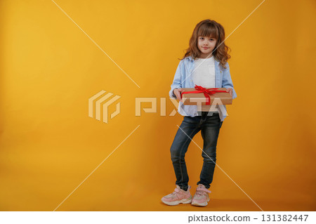 Gift box in hands. Cute little girl is against yellow background 131382447