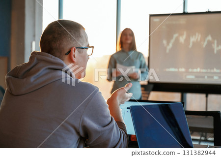 Guy is listening. Female business trainer is against projector with business data, teaching the man Guy is listening. Female business trainer is against projector with business data, teaching the man 131382944