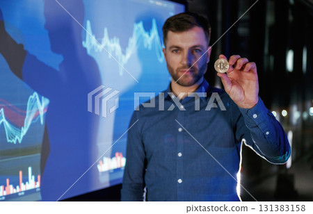 Digital currency, holding coin in hand. Business coach against projector with data Digital currency, holding coin in hand. Business coach against projector with data 131383158