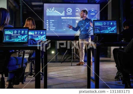 In formal clothes. Male business trainer is against projector with data, teaching people In formal clothes. Male business trainer is against projector with data, teaching people 131383173