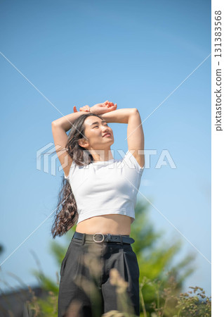 一位長髮年輕女子在藍天下一邊運動一邊聽音樂 131383568