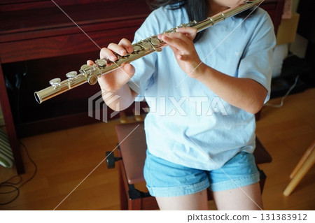 特寫鏡頭：一名六年級小學生坐在室內的椅子上吹笛子，她的手和樂器 131383912
