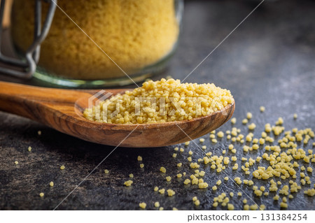 Raw couscous in spoon on black table. Raw couscous in spoon on black table. 131384254