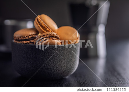 Different flavors of macarons. Colourful macaroons in bowl on black table. 131384255