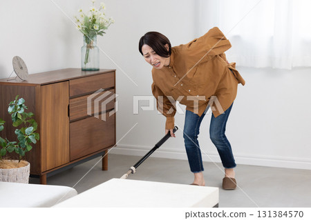 A woman in her 30s who seems to be in pain after hurting her back while cleaning 131384570