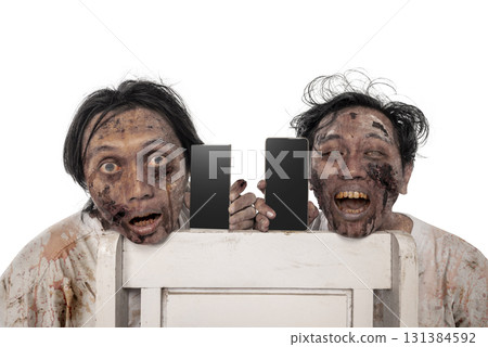 Portrait of two scary male zombies with a wound and blood on their bodies holding a cellphone isolated over a white background. Mockup or Copy space. Spooky expression. Concept of Halloween or Horror 131384592