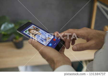 Man looks through a photo of a young European woman on his smartphone, clicks I like it 131384737