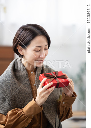 A middle-aged woman smiling with a gift box in her hand A middle-aged woman smiling with a gift box in her hand 131384841